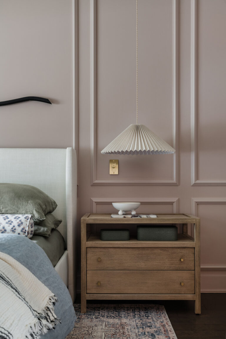 Primary bedroom with meadow pink walls, picture molding, pleated hanging pendants, brass dimmer and styled nightstand.