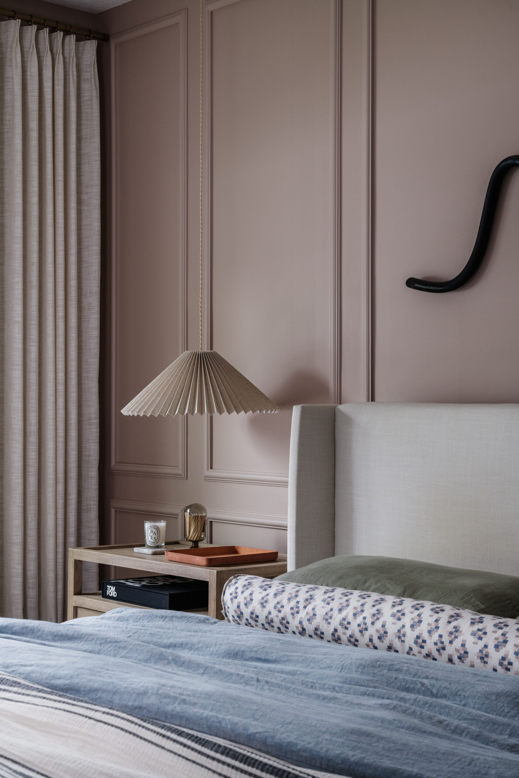 Primary bedroom with meadow pink walls, picture molding, pleated hanging pendants, custom bolster, eclectic linens and styled nightstand with dramatic floor-to-ceiling and wall-to-wall pinch pleat linen drapery.