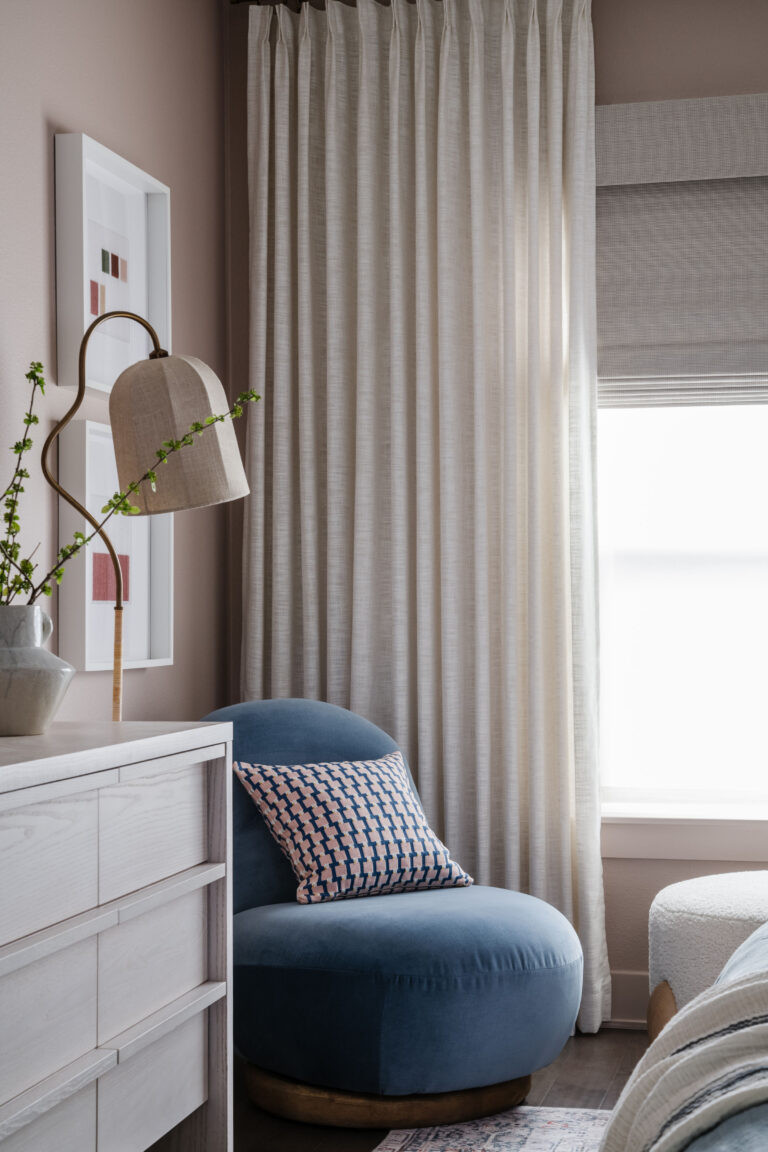 blue velvet chair vignette with graphic pillow, dresser, statement floor lamp, and dramatic floor to ceiling drapery