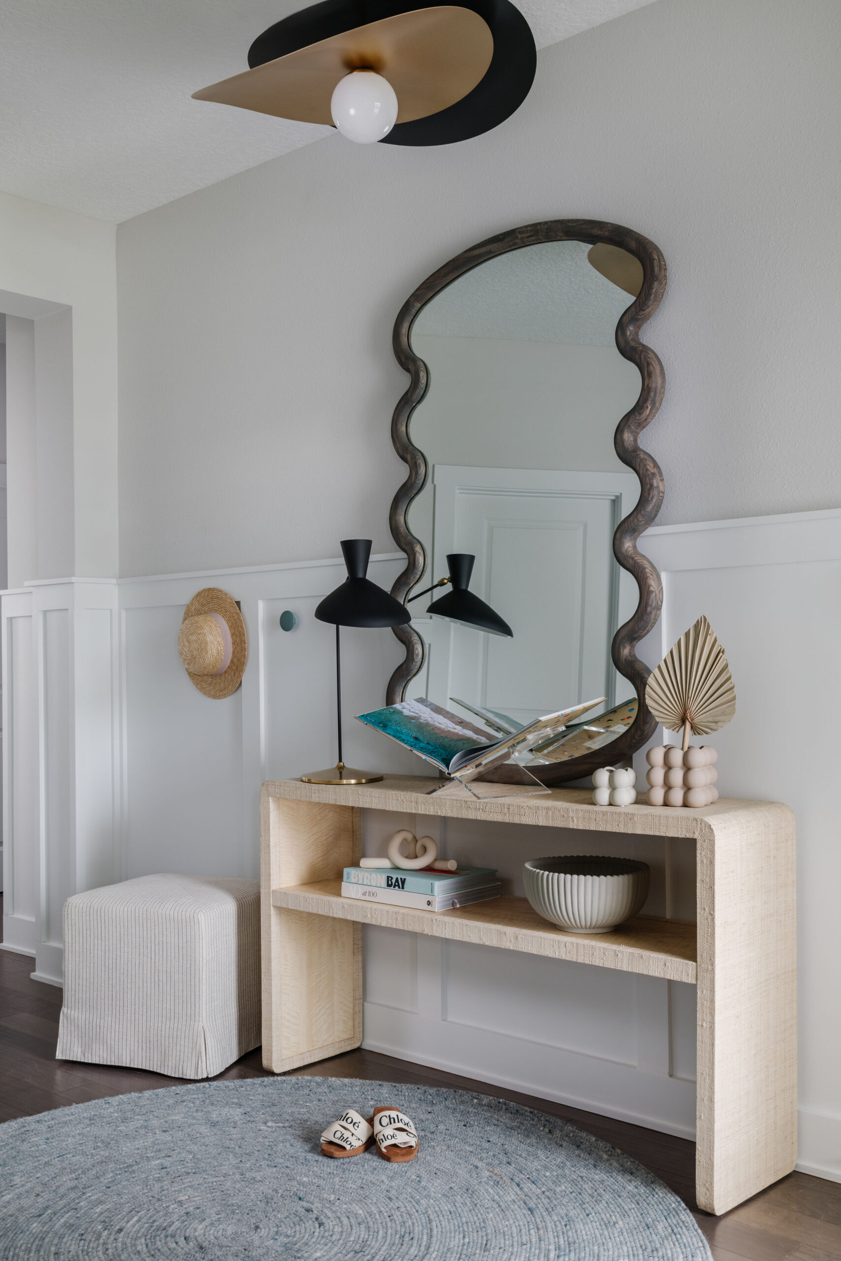 Entry vignette with wavy mirror, styled console table, round rug and ottoman.