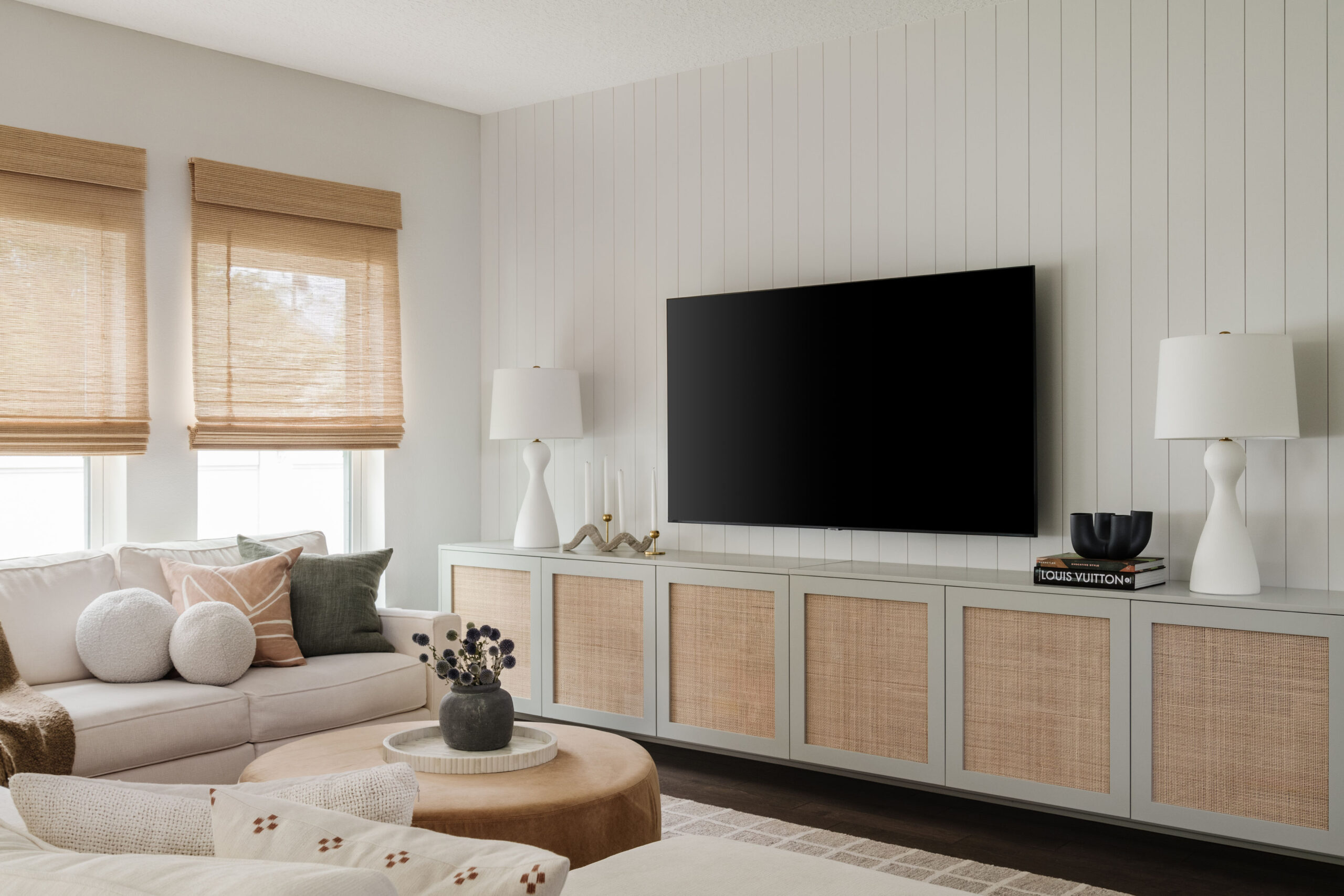 TV wall with floating console, pair of matching lamps, ottoman and sofa with a variety of pillows.